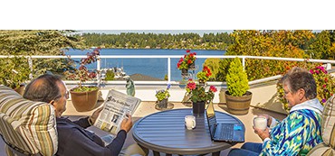 Senior residents on the deck reading the newspaper and working on laptop