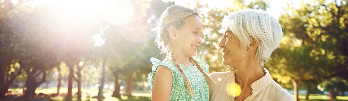 Senior woman holding granddaughter outside with sun shining